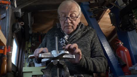 senior male mechanic using file to work on a machine part in old workshop