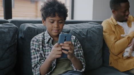 boy using smartphone on a couch with his father and a pet