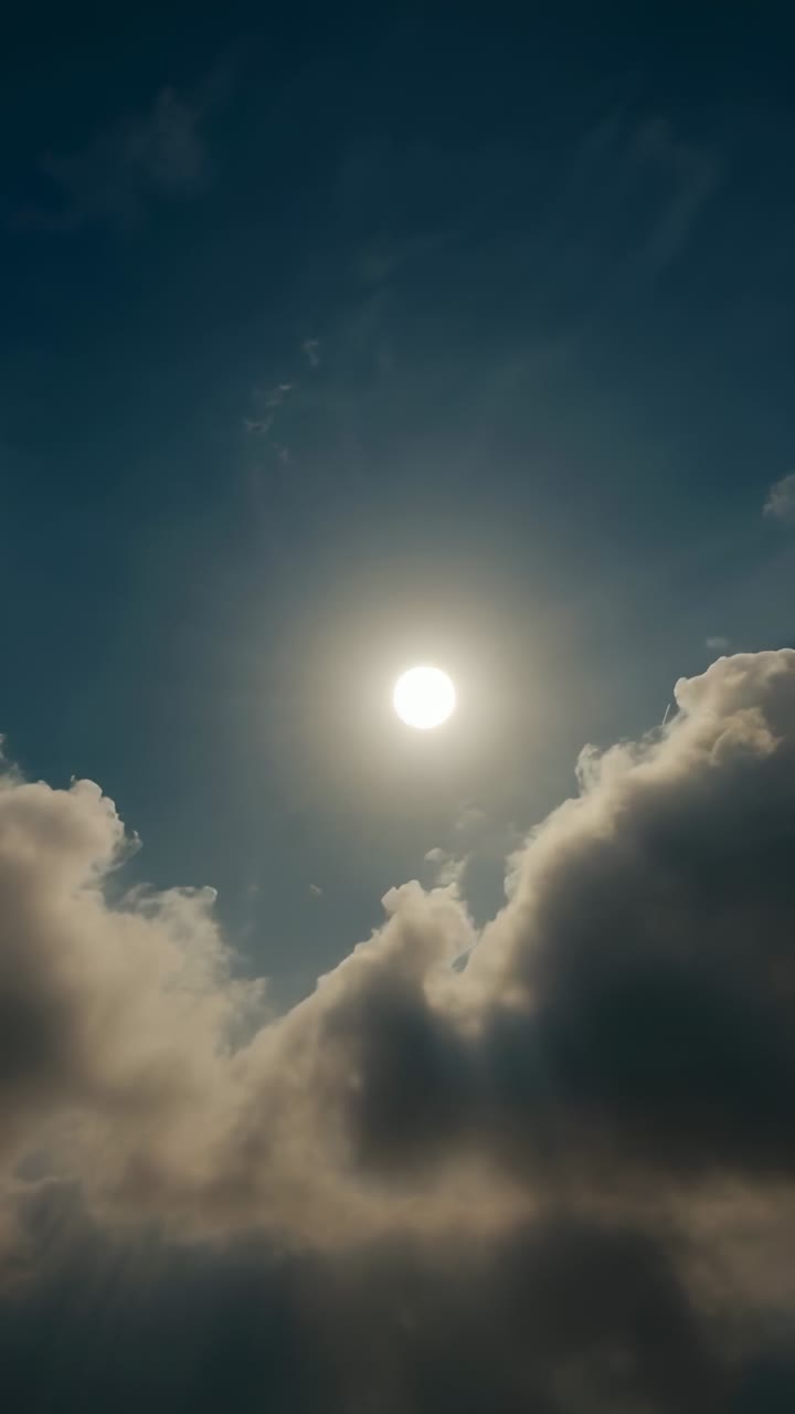 Vertical video: Drifting cumulus and cirrus clouds passing over sun in sky, being carried by breeze