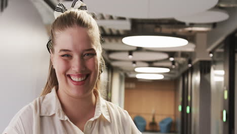 smiling woman in office hallway, wearing white shirt and striped hair bow