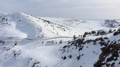 Vista-Por-Drones-De-Un-Automóvil-Que-Pasa-Cruzando-Una-Carretera-De-Montaña-A-Gran-Altitud-Hermosas-Laderas-Cubiertas-De-Nieve-El-Día-De-Invierno