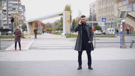 portrait of a man having a phone talk outdoors. handsome businessman in suit and warm coat stands on the city street uses mobile phone. slow motion.