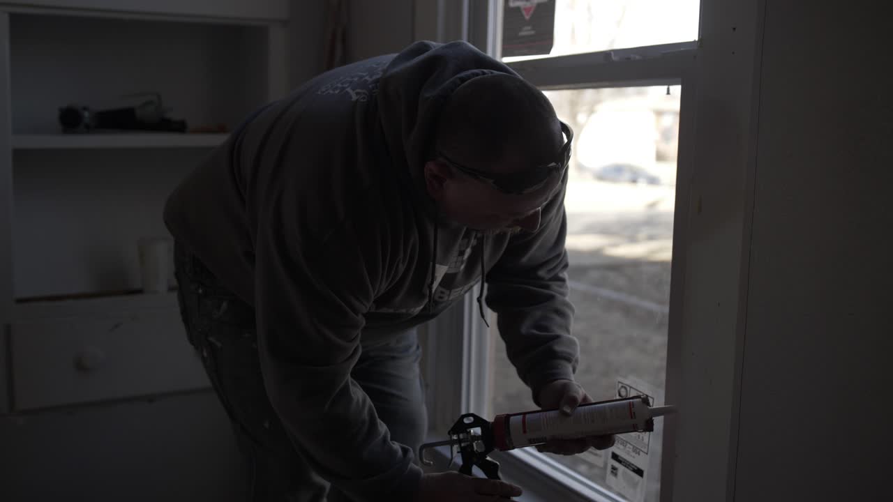 A man works inside remodeling a house - seals window trim-1