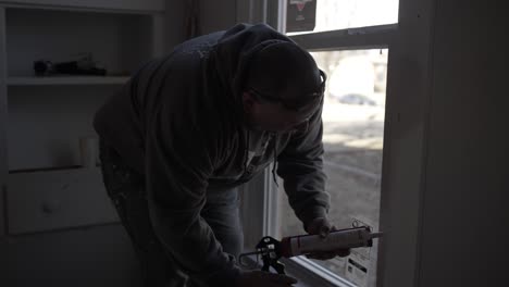 a man works inside remodeling a house - seals window trim-1