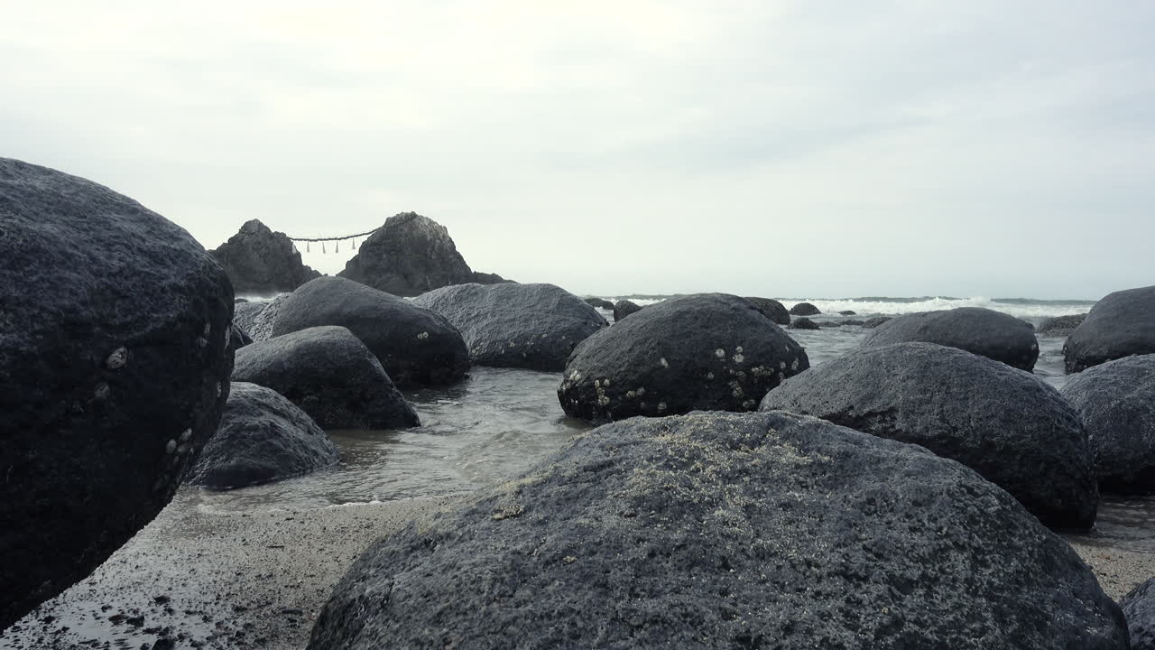 Sea   water getting between rocks reaching the sand on the shore of a beach with the ocean and a mountain background close up shot