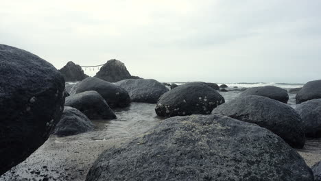 sea   water getting between rocks reaching the sand on the shore of a beach with the ocean and a mountain background close up shot