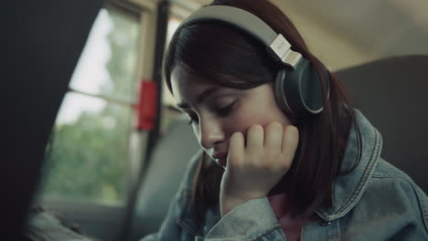 Closeup-upset-girl-sitting-schoolbus-alone-with-headphones-waiting-for-ride.