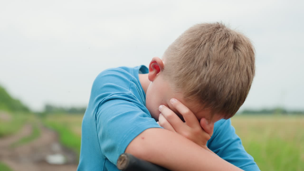 들판에 앉아 있는 백인 소년, 자전거는 세워져 있고, 흐린 여름 하늘, 흙길과 키 큰 풀, 생각에 잠긴 듯하다가 얼굴을 가리며, 고독과 감정을 담은 친밀한 묘사, 자연광