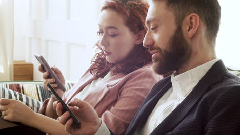 mujer y hombre con ropa formal usando teléfono móvil y hablando juntos mientras están sentados en el sofá 1