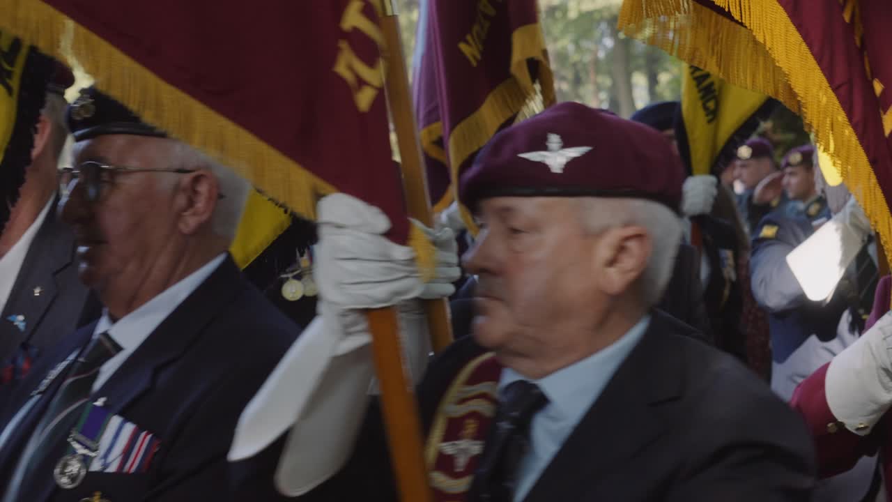 Veterans, proudly carrying maroon military flags, march in unison during a military commemoration. The image captures the solemnity and honor of the occasion as they pay tribute to their service