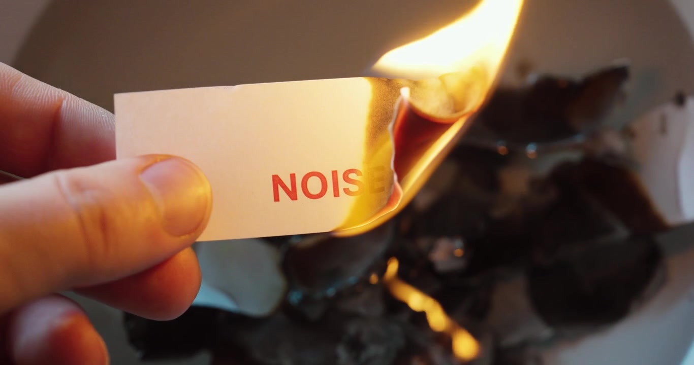 Close-up of paper labeled “noise” being burned, symbolizing removal of distractions and focus on clarity.