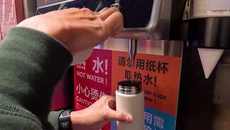 person fills bottle from hot water dispenser