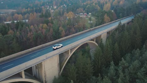 electric car on elevated bridge, tracking drone shot of white vehicle moving on road on humid autumn day