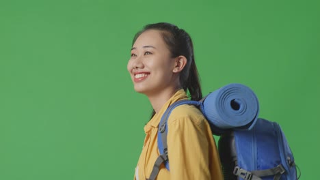 close up side view of asian female hiker with mountaineering backpack walking on green screen background in the studio