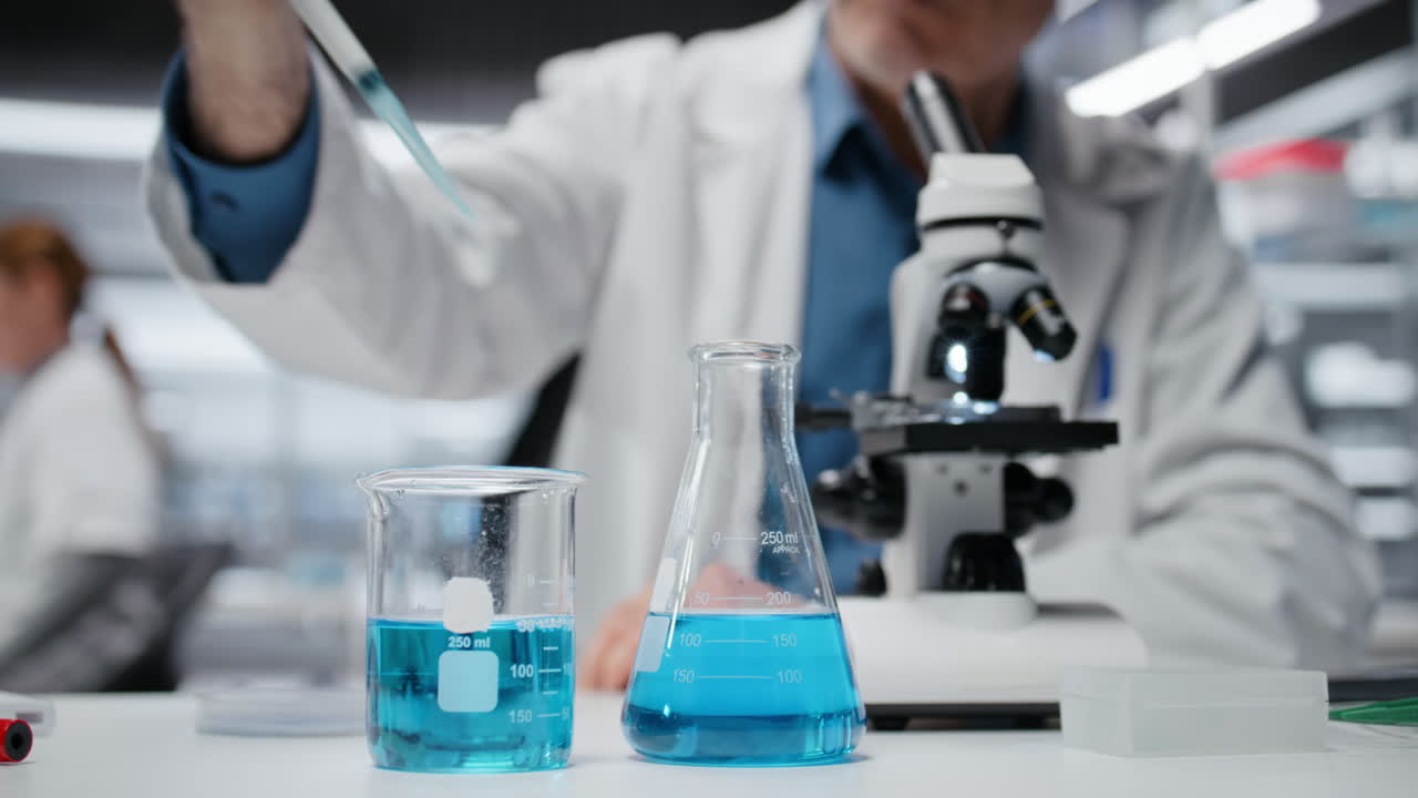 Ingegnere chimico anziano che pipetta un liquido blu in una provetta.