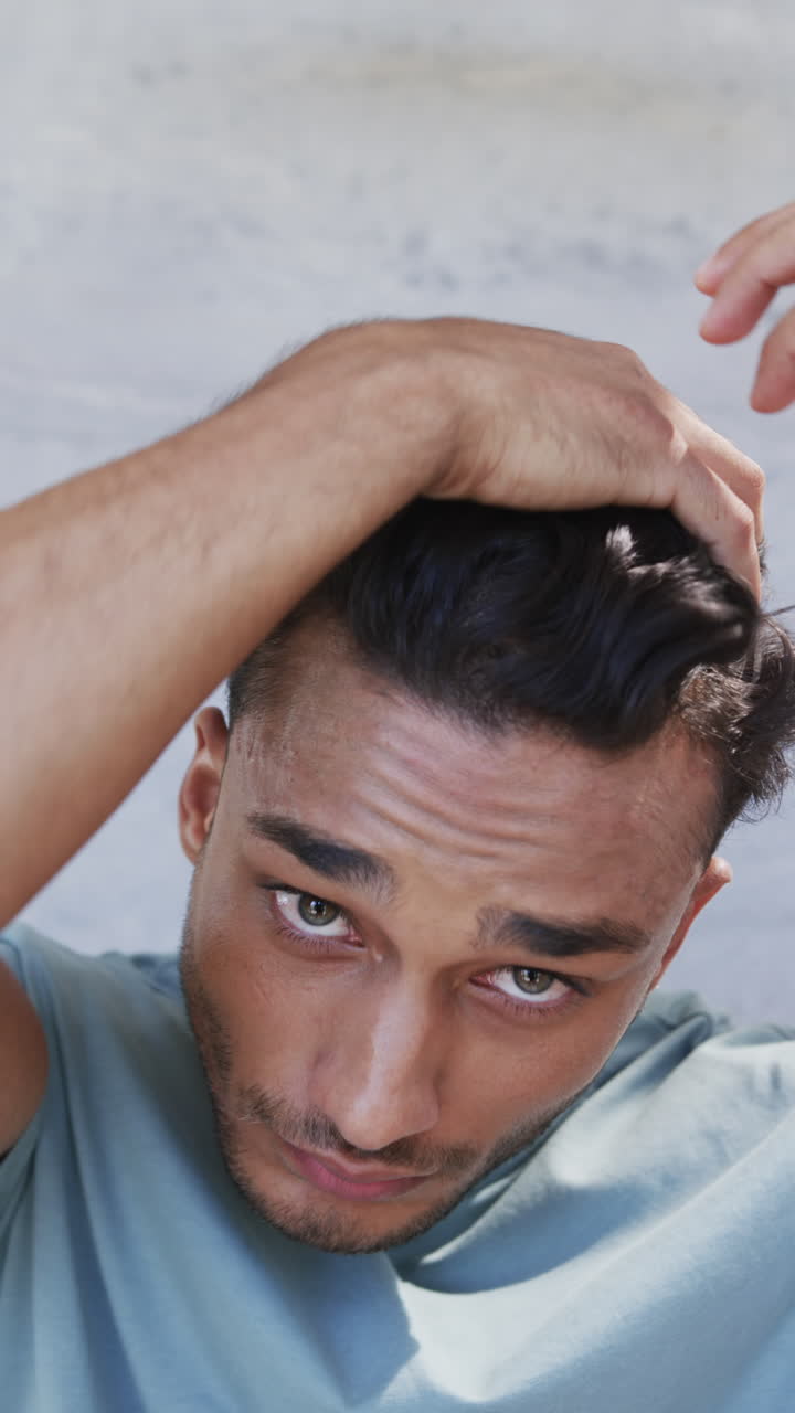 Vertical video of happy latino man arranging hair and smiling in sunny bathroom