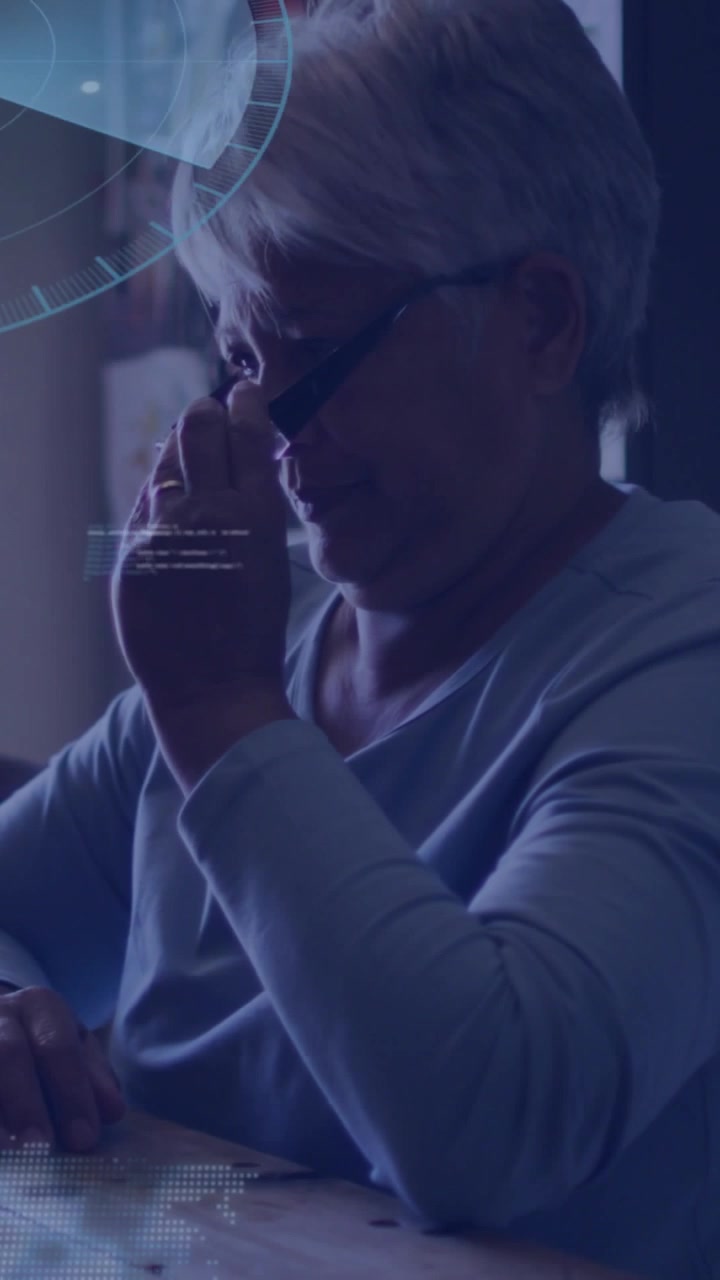 Vertical video: Woman at table rubbing eyes and fixing glasses as health HUD appearing to read data