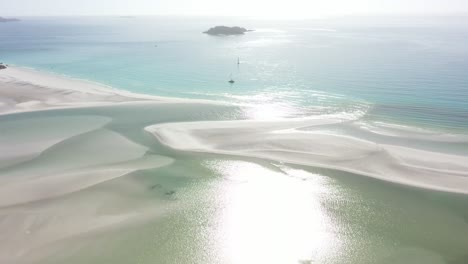 Rotierende-Sonnenstrahlantenne-über-Flacher-Sandlagune,-Dahinter-Segelboote