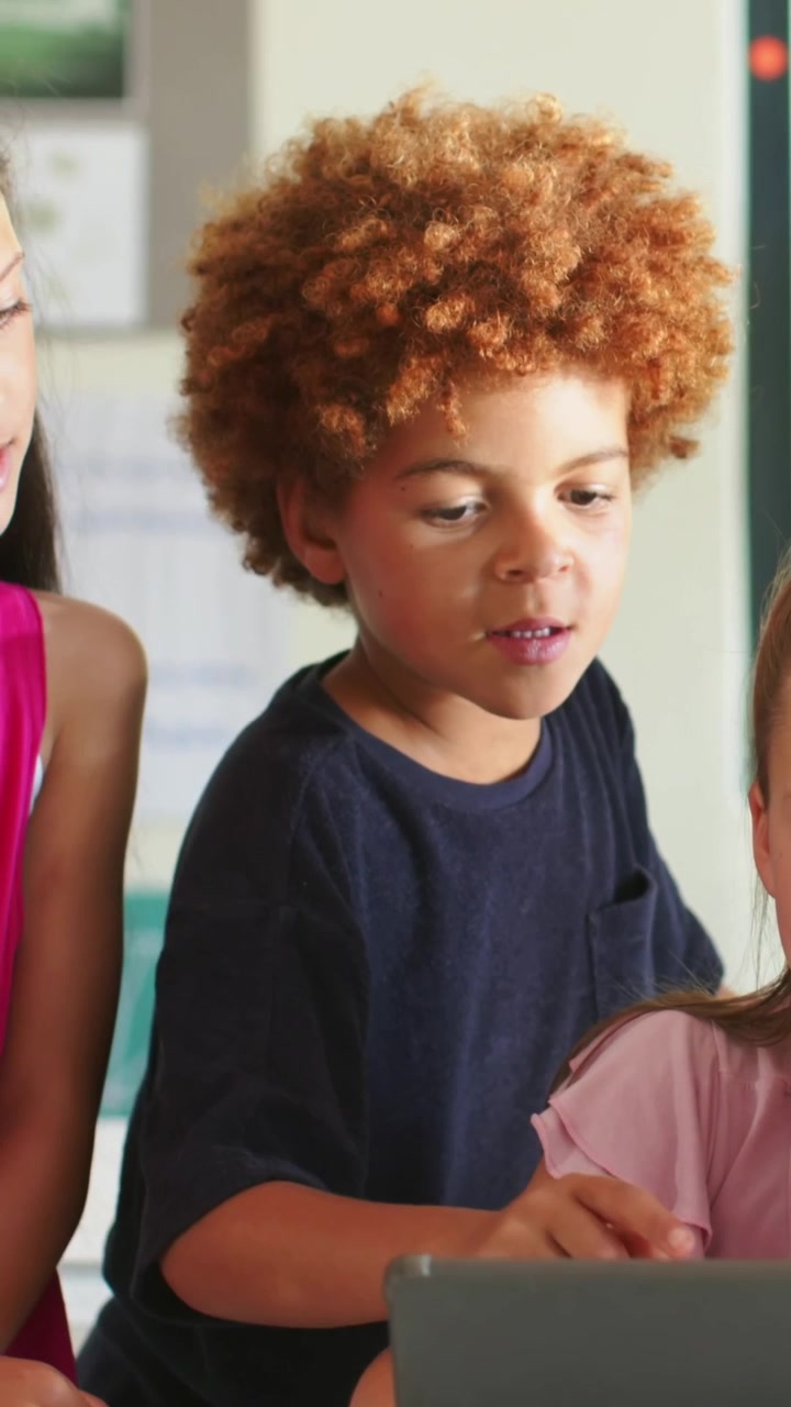Vertical video: curly boy leaning forward pointing at laptop while seeing error and helping friends