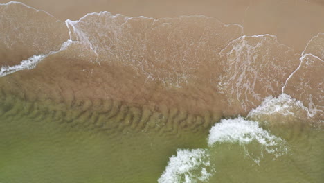 aerial: medium shot of top view shot of waves crashing on the shallow shore and spilling on sand