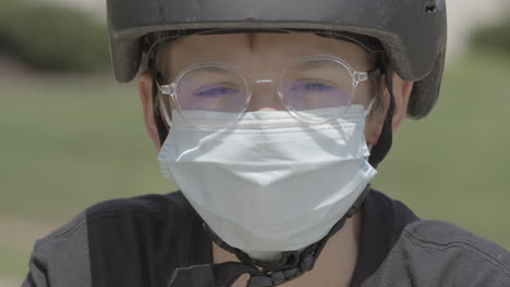 portrait d'un adolescent à l'extérieur portant des lunettes, un casque de vélo et un masque médical