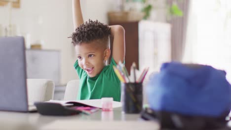 happy african american boy sitting at table, using laptop for online lesson