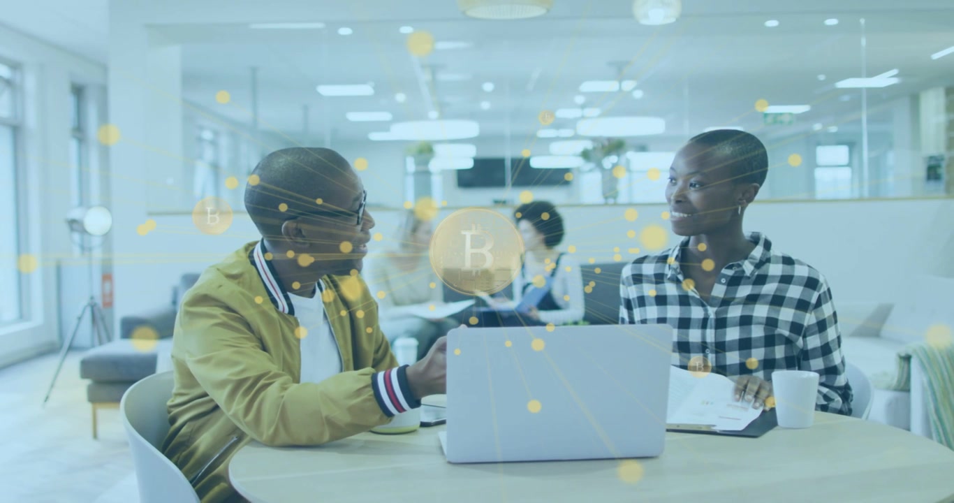 Two coworkers pointing at laptop, particles forming coin icons floating between them for finance