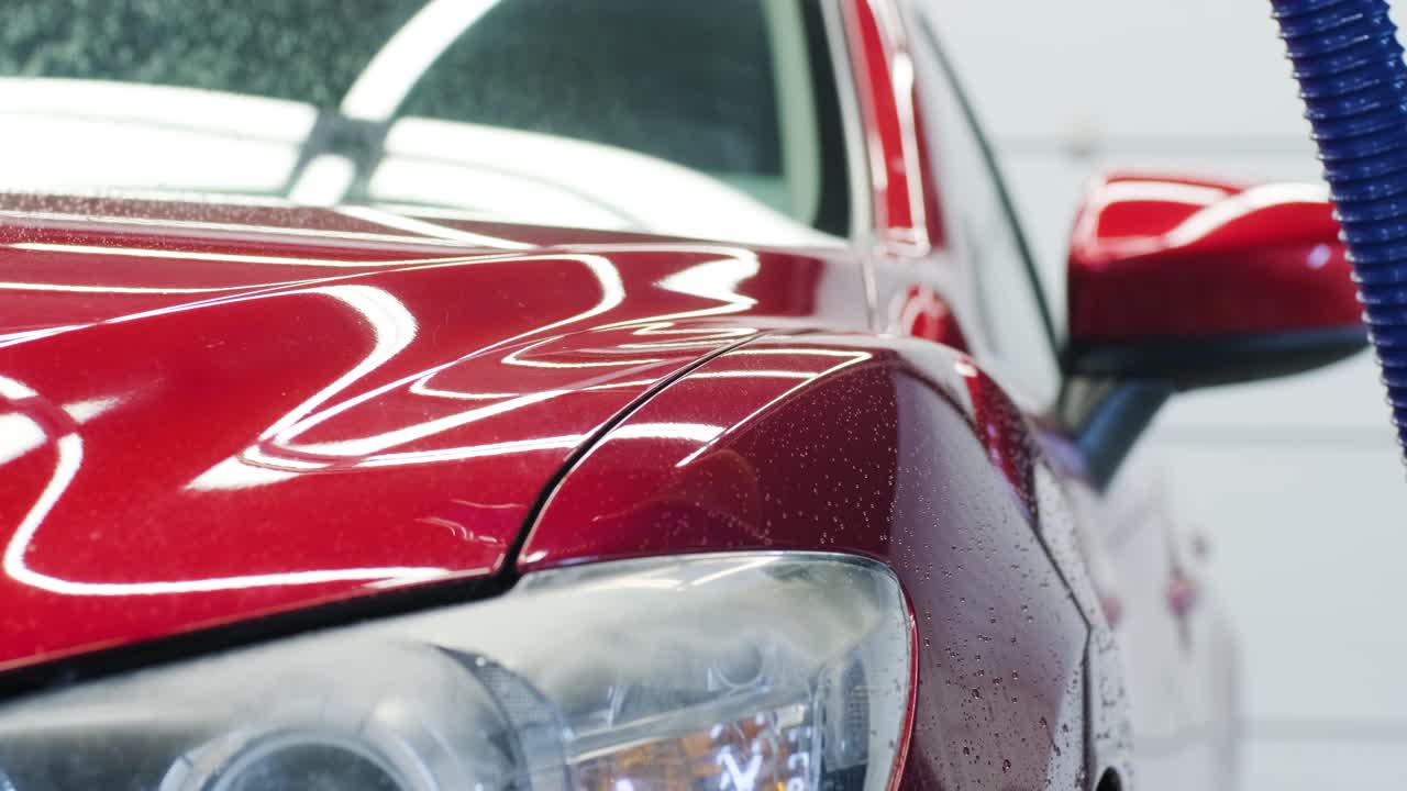 Lavaggio auto con schiuma e acqua ad alta pressione. Auto rossa.