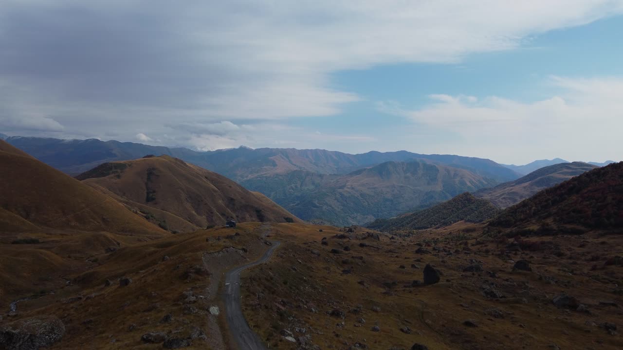 Drone fly at winding dirt road leading through bare hills and valleys under cloudy sky, Khevsureti, Mtskheta-Mtianeti, Georgia