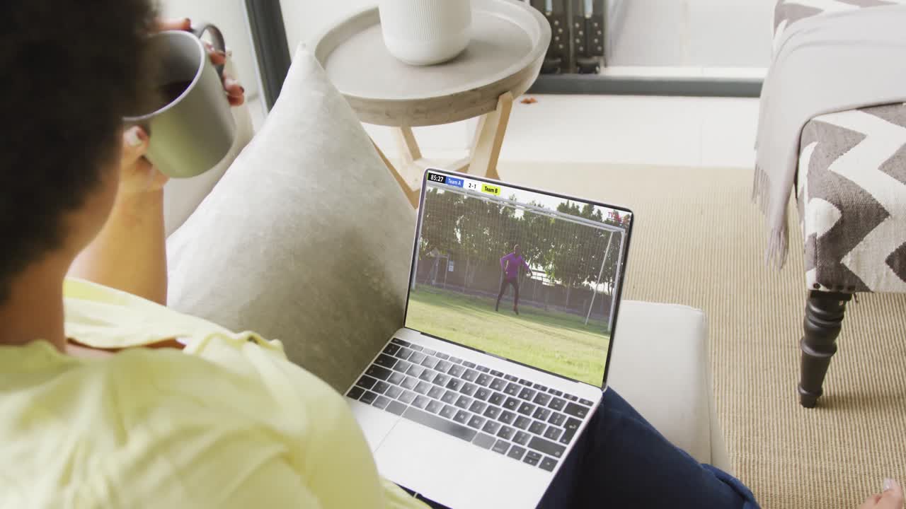 African american woman using laptop with male soccer player playing match on screen