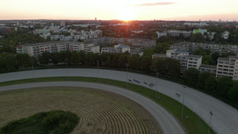 Harness-Racers-on-Dirt-Horse-Race-Track-in-Berlin,-Germany-at-Sunset,-Aerial-follow-tracking-Shot-from-above