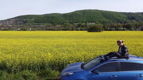 Freizügiger,-Erschossener-Mann,-Der-Entspannt-Auf-Dem-Dach-Eines-Blauen-Autos-In-Einem-Leuchtend-Bunten-Gelbgrünen-Blumenfeld-Sitzt