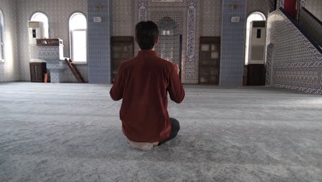 back view of a young bearded man sitting inside mosque praying to god with open hands, muslims who go to historical and holy places pray