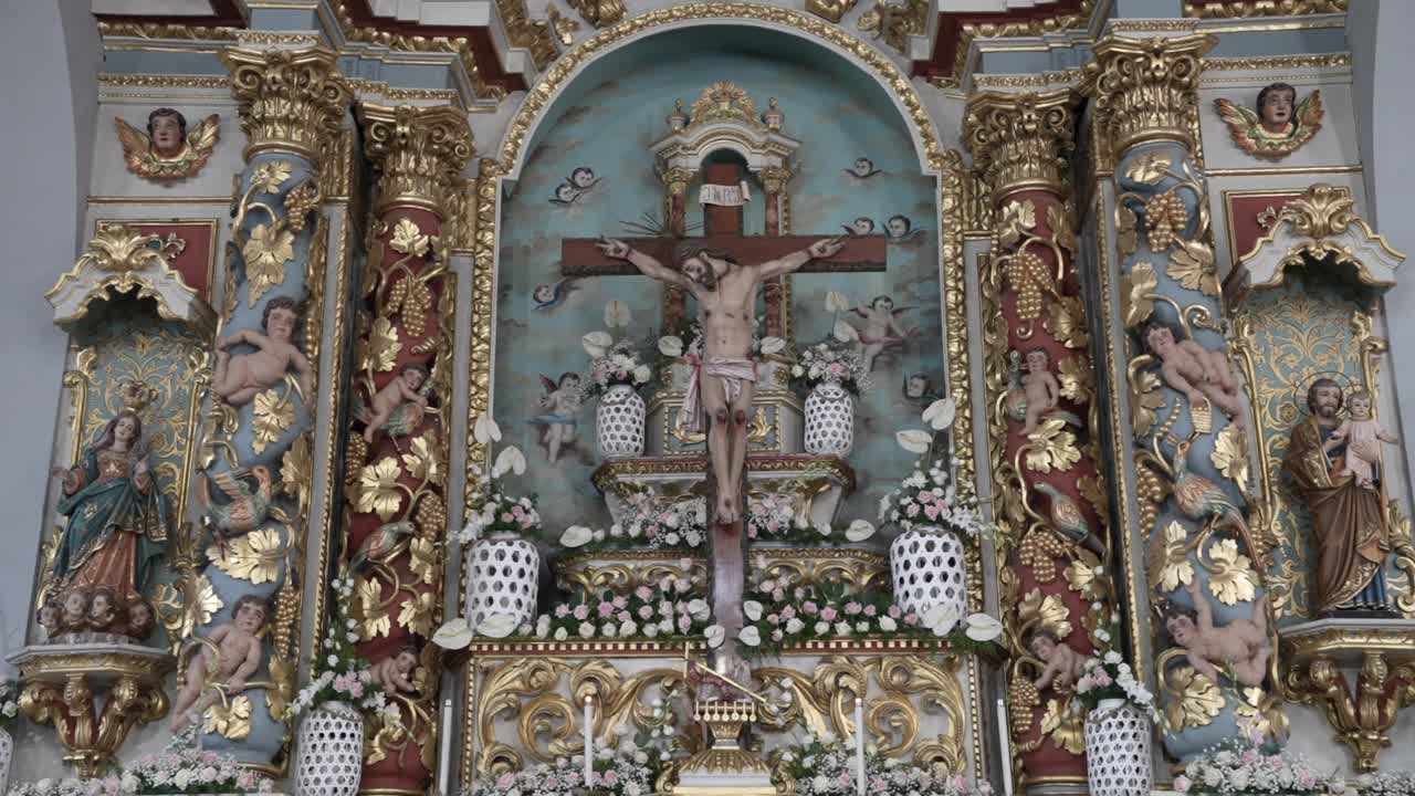 Altare barocco di chiesa con crocifisso di Gesù Cristo, circondato da intagli dorati ornamentali, angeli, decorazioni floreali e statue sacre