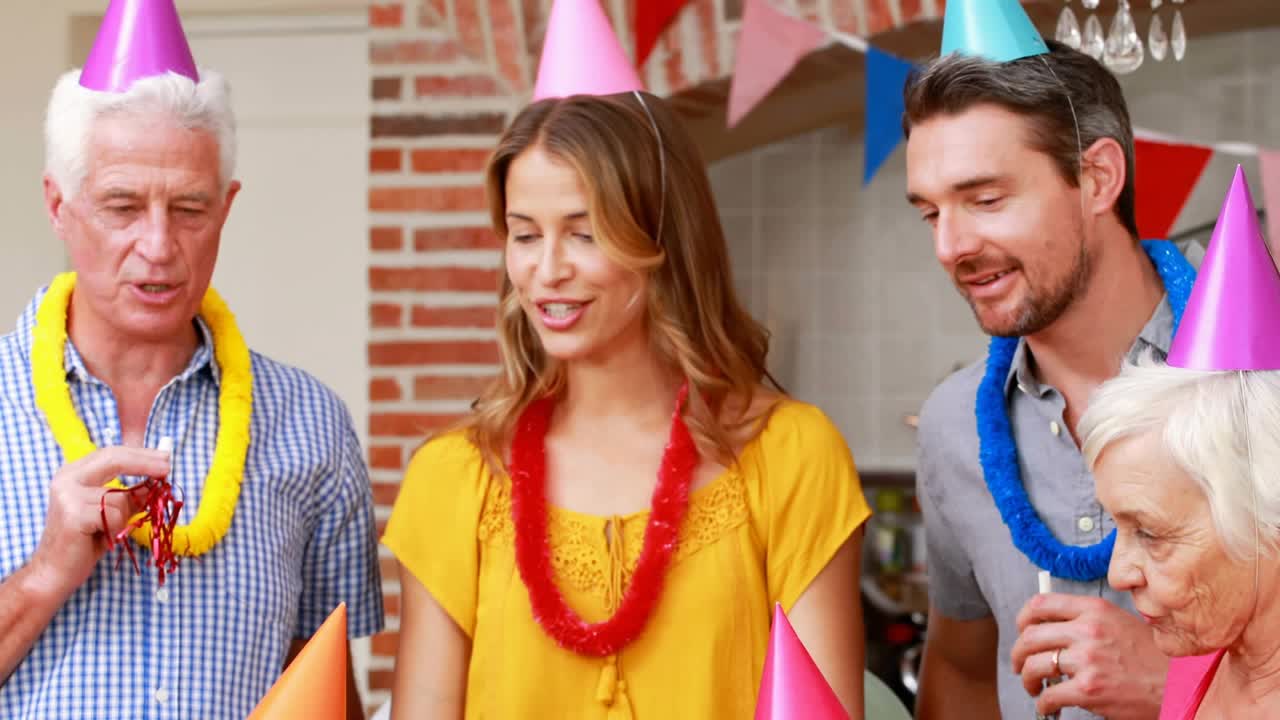 Children blowing lit candles on cake at party table, senior using horn starting animated confetti