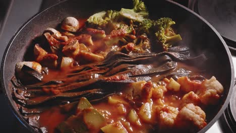 noodles, vegetables and chicken breast is simmering in sauce in the pan