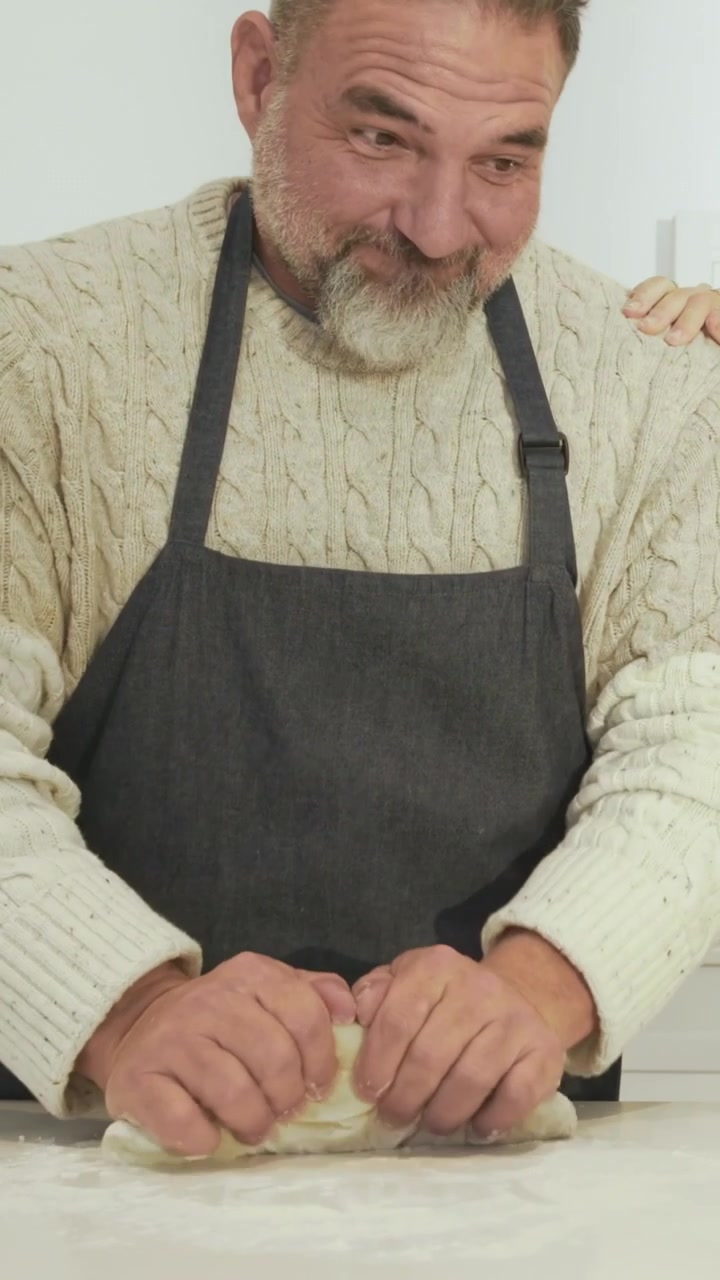 Vertikales Video: Nimmt Kugel auf, Mann in Schürze knetet Teig auf der Küchenarbeitsplatte, mit Rührschüssel.