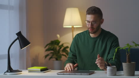 Un-Hombre-Exhausto-Está-Terminando-De-Trabajar-Con-Una-Computadora-Portátil-Por-La-Noche-En-Casa-Cerrando-Un-Cuaderno-Y-Quitándose-Las-Gafas-Frotándose-Las-Sienes,-Dolor-De-Cabeza-Y-Fatiga