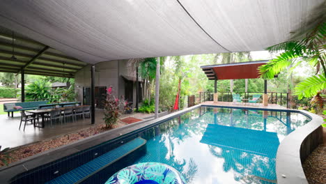 rural prestigious tropical style home pool and deck area with tropical inflatable ring floating as water reflects trees and leafy greens