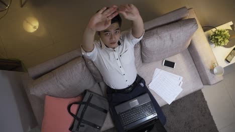 high angle shot chinese businessman working overtime at home is looking upward smiling with spread arms and hands behind head after getting job done on computer