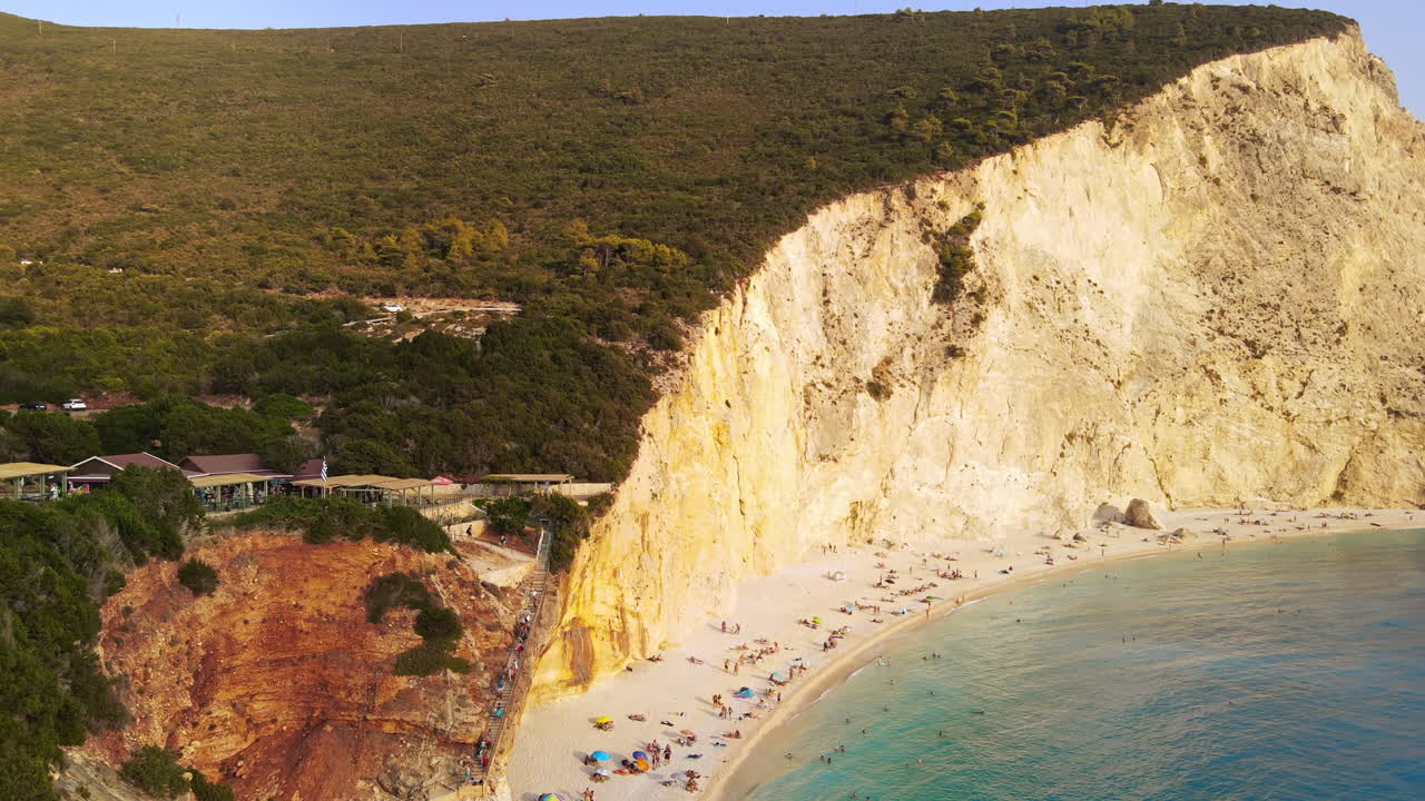 Aerial drone view of the Ionian Sea coast of Zakynthos, Greece. Rocky cliff, vegetation, beach with resting people, blue water. Sunset