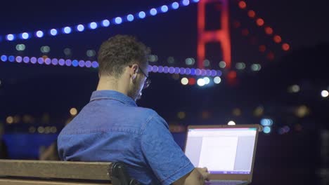 hombre trabajando en una computadora portátil contra la vista nocturna del mar.