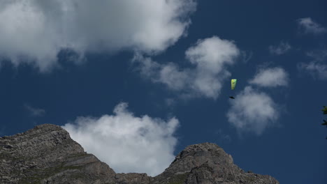 a yellow parachute is flying over rocky mountain peaks in the swiss alps in a cloudy sky, engelberg, obwalden