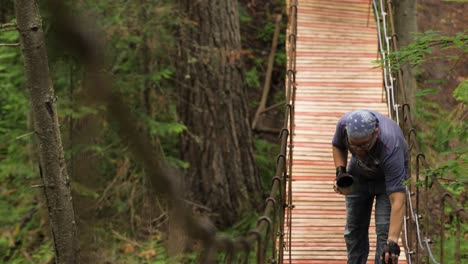 man walking on a wooden suspension bridge in a forest