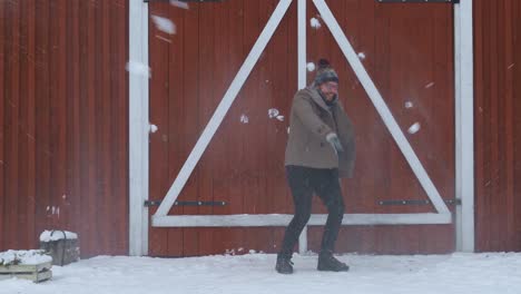 man dodging snowballs in slow motion near a red house in norway