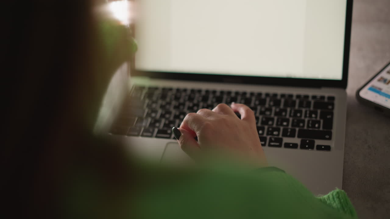mujer con un suéter verde escribiendo en una computadora portátil, capturada con una cámara de mano. la escena hace hincapié en un estado de ánimo de trabajo enfocado, destacando la productividad y el trabajo digital moderno