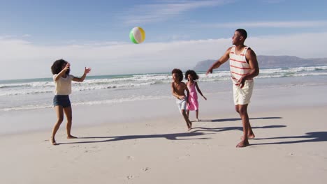 padres afroamericanos y sus hijos jugando con una pelota en la playa