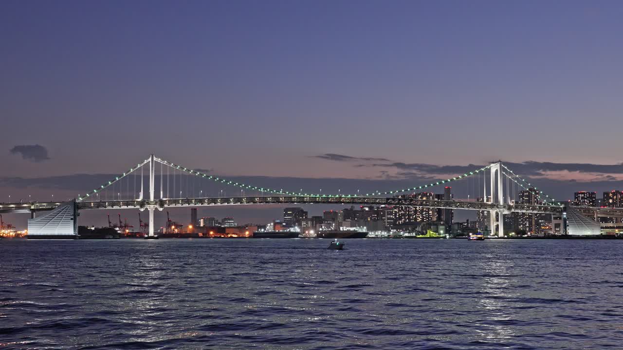 Close-up view of the iconic Rainbow Bridge illuminated at night, spanning Tokyo Bay with city lights behind