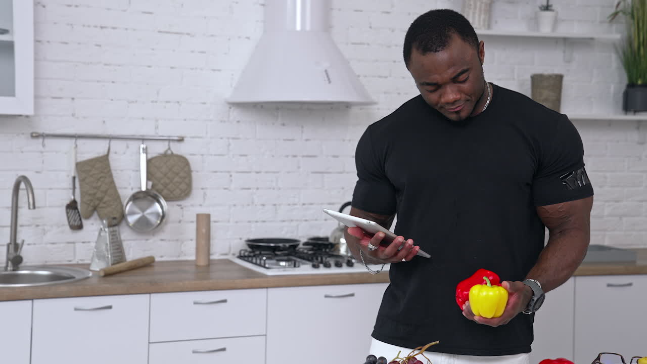 Multiracial man in kitchen ready to prepare meal with vegetables and fruits. Guy is holding pepper. Kitchen background. Healthy food. Vegans and vegetarians