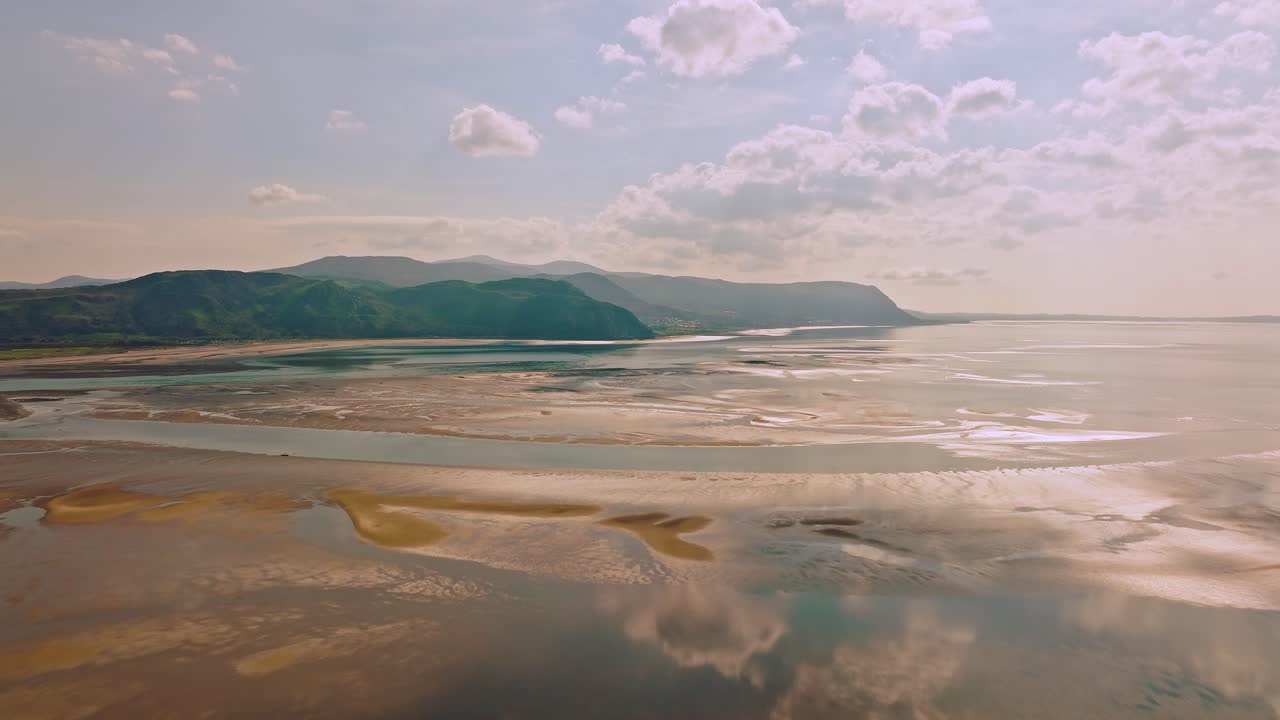 Beautiful reflection of the white clouds with the blue sky in the slowly rising water after low tide as the shadows of a cloud slide over the sand colored mud off the coast of Wales